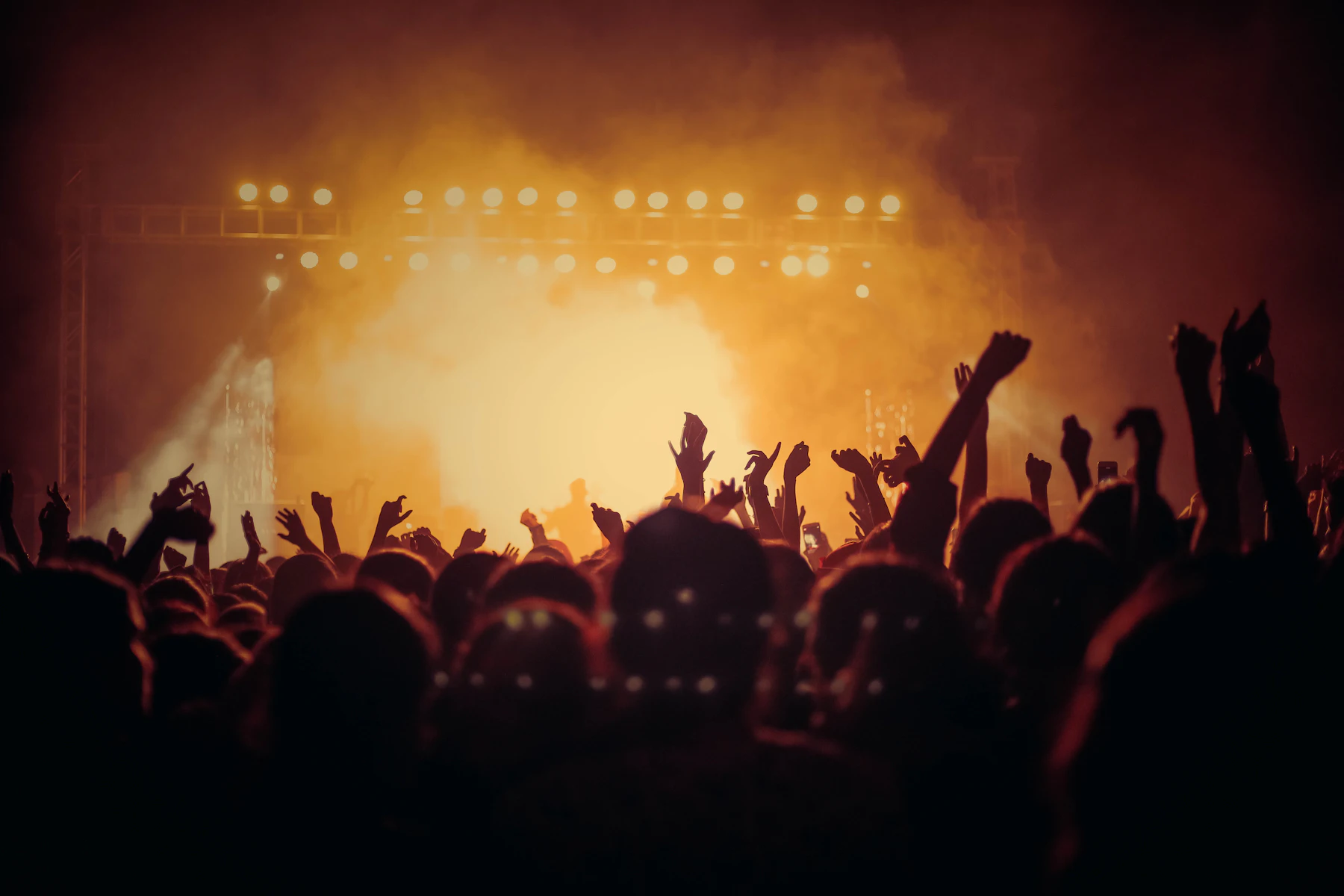 A packed concert crowd raising their hands beneath amber stage lights