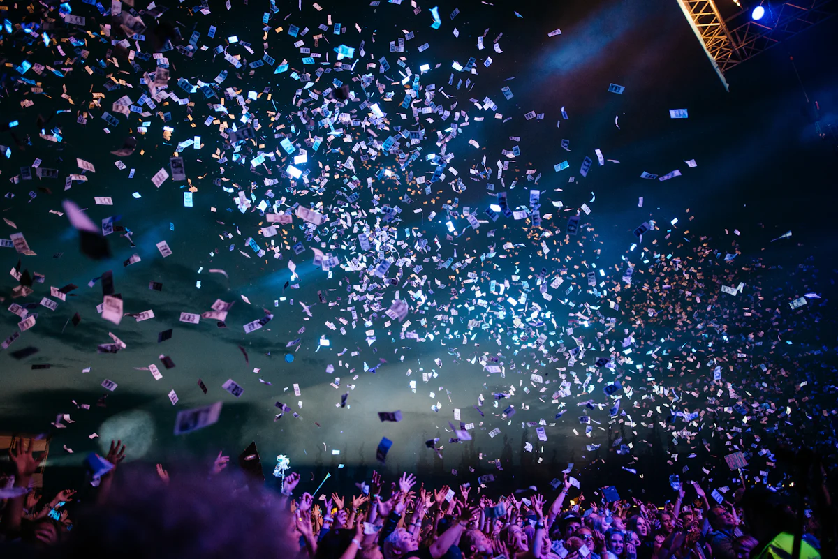 A large festival crowd reaching toward a stage while confetti fills the air